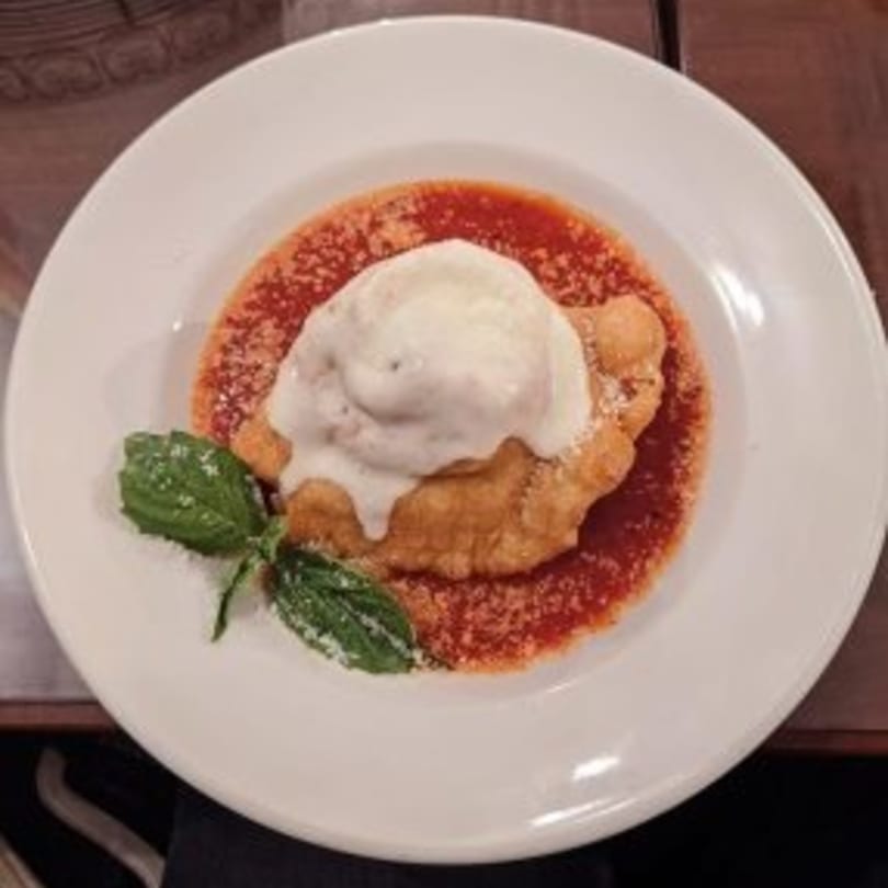 Fried dough dessert with vanilla ice cream, tomato sauce, and basil on a white plate.