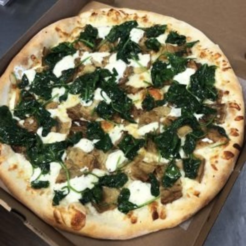 Mangia Pizza's white pizza with spinach, ricotta cheese, and roasted garlic in a cardboard box.